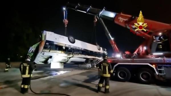 A crane lifts the bus wreck  as firefighters look on.